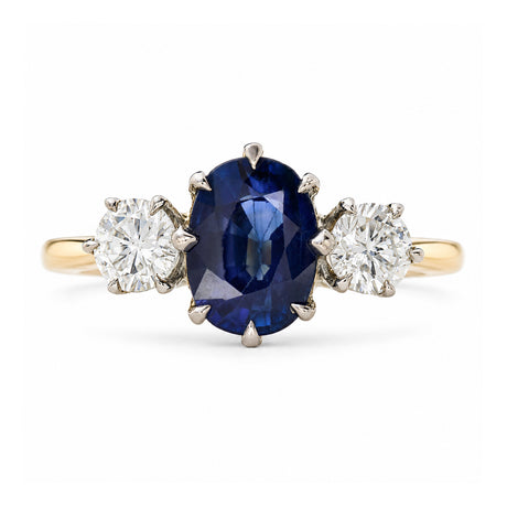 A yellow gold Antique, Art Deco sapphire and diamond three-stone engagement ring set on a plain white background.