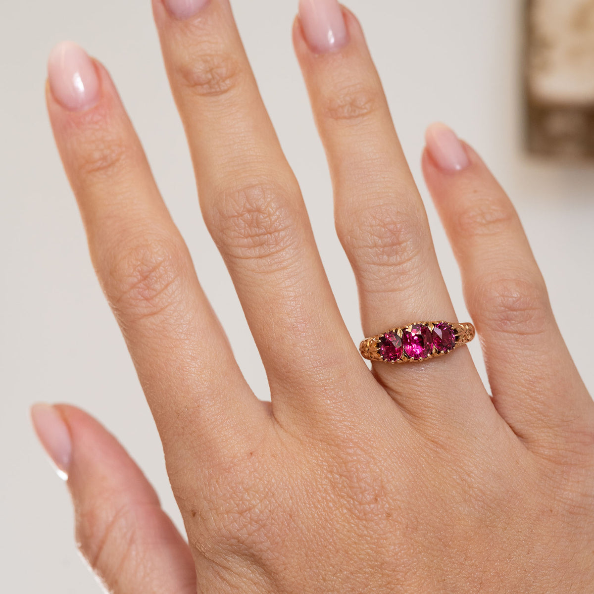 Edwardian three-stone ruby engagement ring worn on the hand, displaying its vibrant colour and elegant antique proportions.