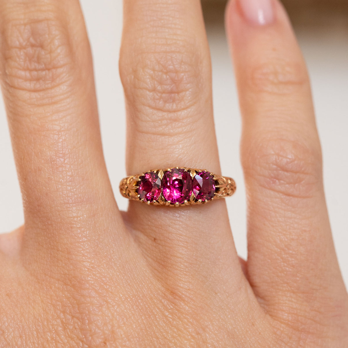 Close-up on-hand view of the Cambodian ruby trilogy ring, framed by decorative Edwardian scrollwork.