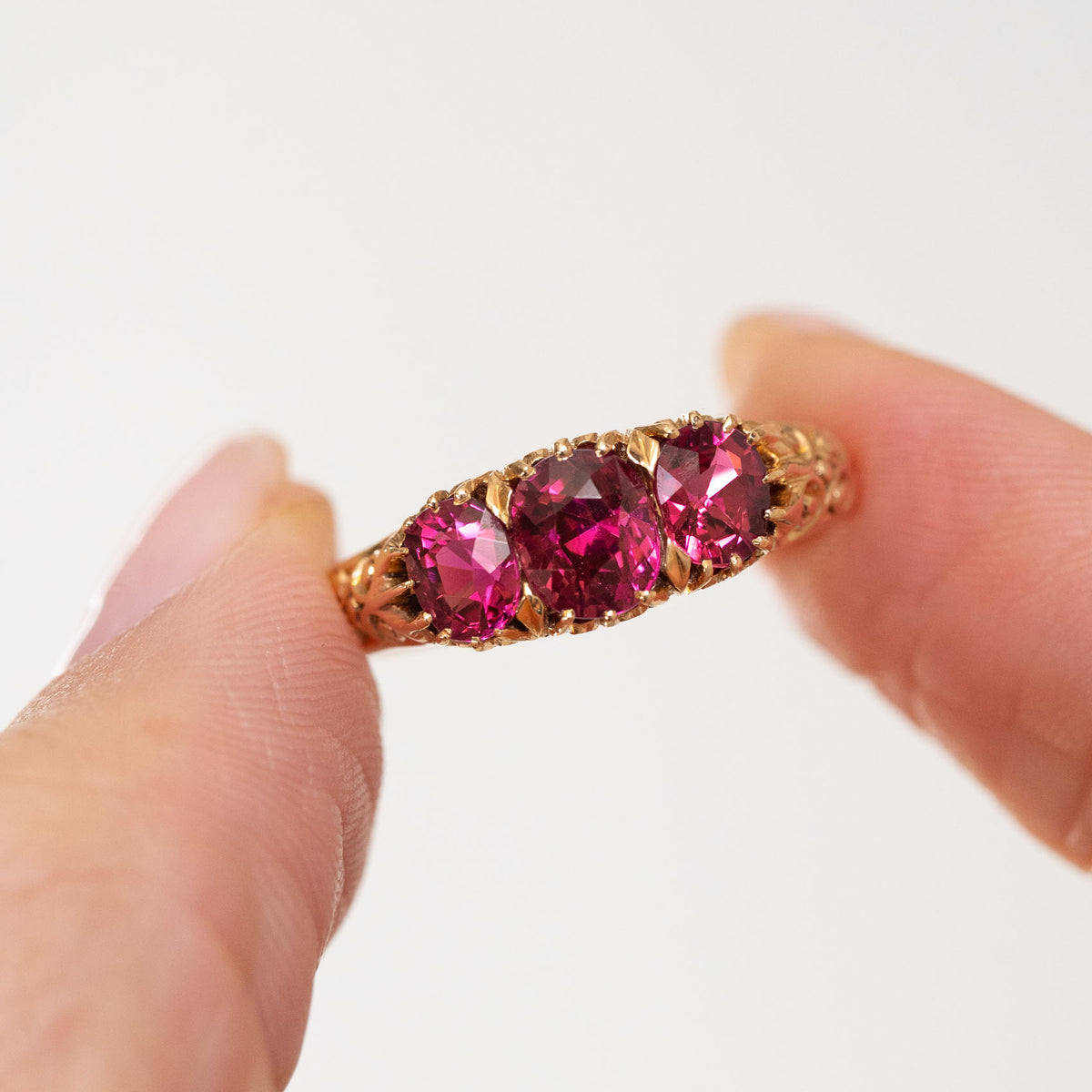 Antique yellow gold ruby ring held between the fingers, offering a clear view of the graduated cushion-cut gemstones.