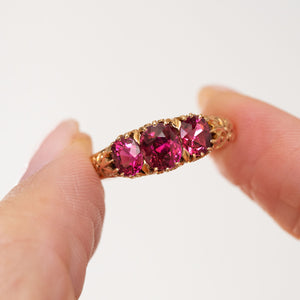 Antique yellow gold ruby ring held between the fingers, offering a clear view of the graduated cushion-cut gemstones.