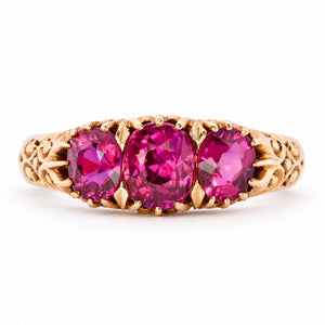 Antique Edwardian Cambodian ruby three-stone engagement ring in yellow gold, set with three graduated cushion-cut rubies and ornate scrolling shoulders.
