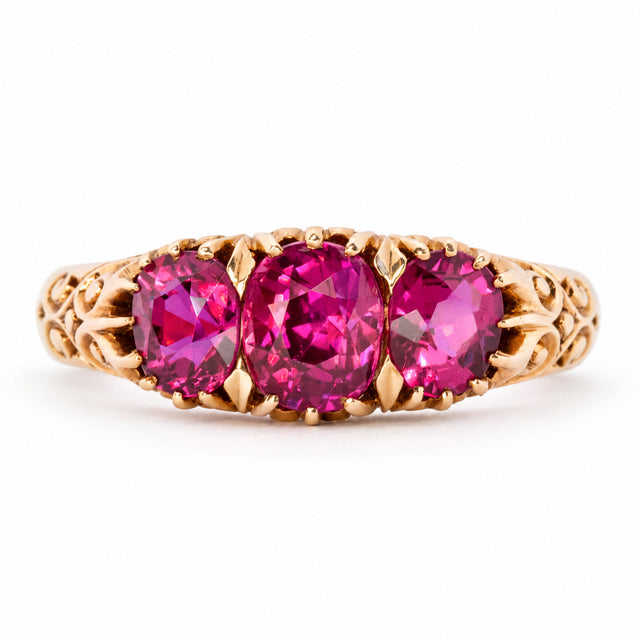 Antique Edwardian Cambodian ruby three-stone engagement ring in yellow gold, set with three graduated cushion-cut rubies and ornate scrolling shoulders.