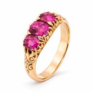 Three-quarter studio view of the Edwardian ruby ring, showcasing its richly carved yellow gold setting and vivid three-stone arrangement.