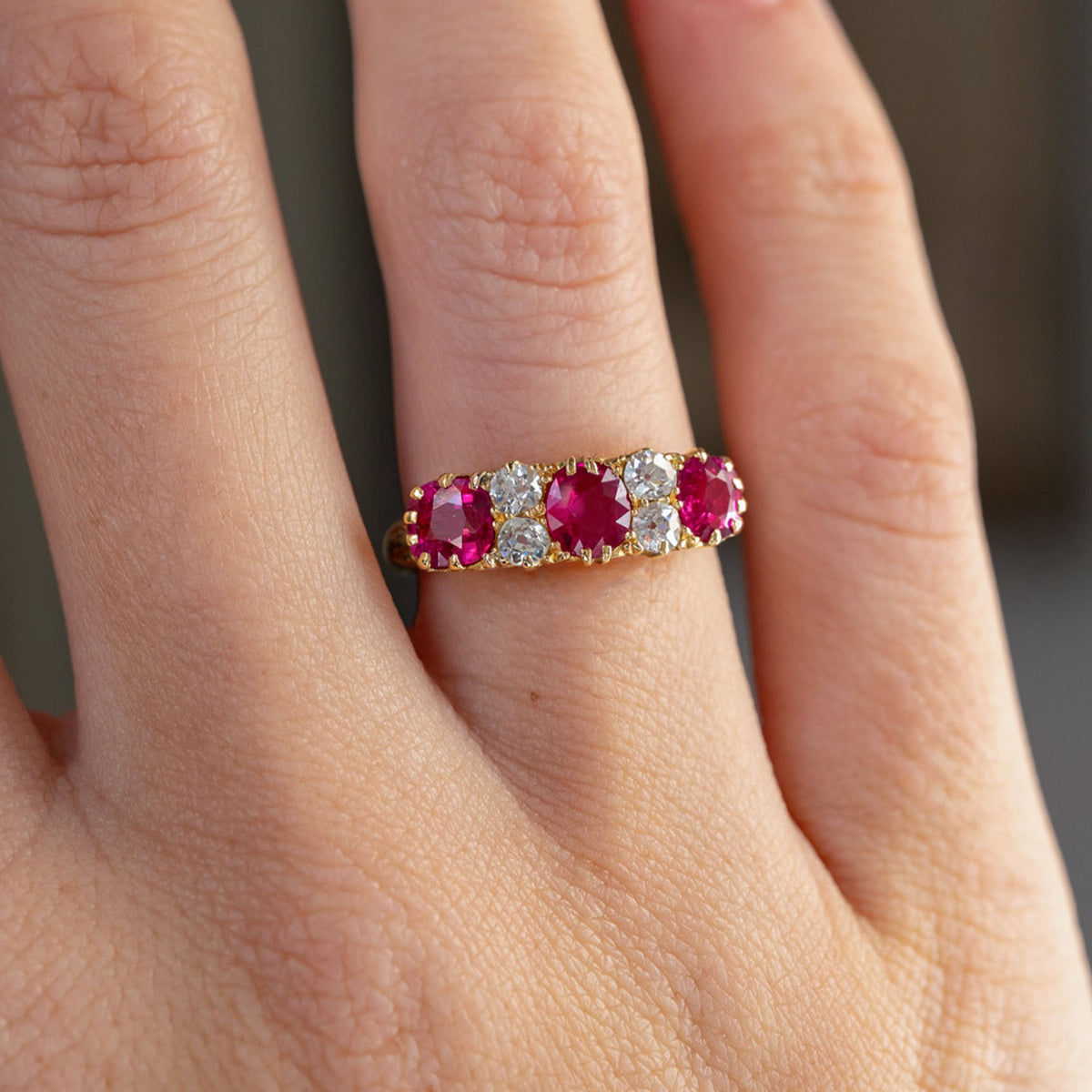 Detailed finger view highlighting the vibrant ruby centres, old-cut diamond accents and scalloped gold setting.