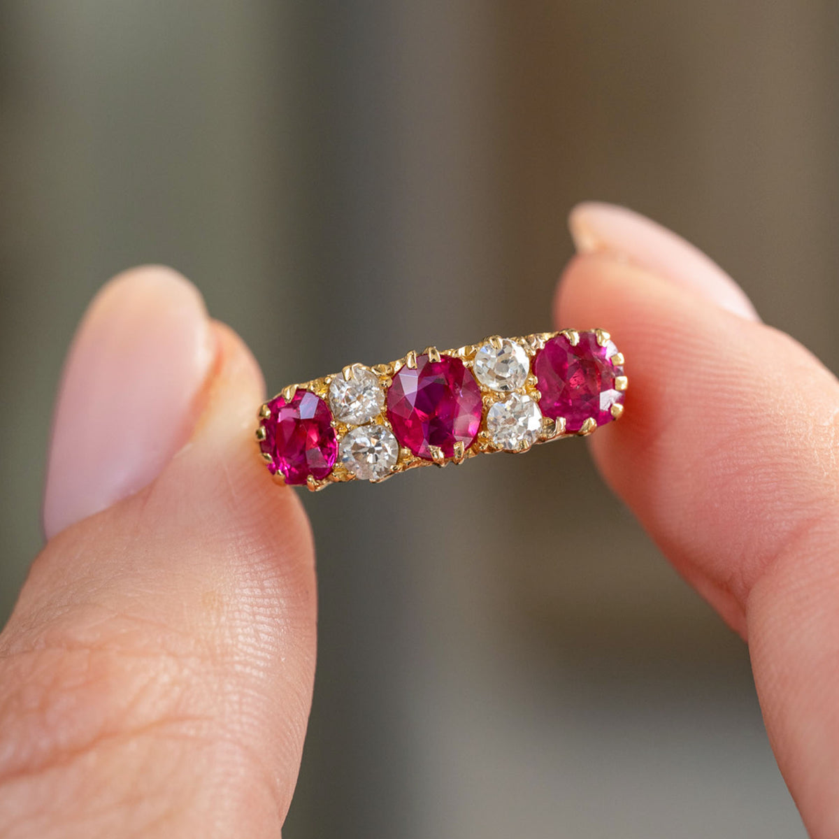 Handheld close-up of the antique five-stone ring, showcasing rich Burmese rubies accented by sparkling old-cut diamonds.