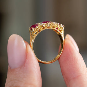 Profile view of the Edwardian ring, displaying the decorative scrolling gallery beneath the rubies and diamonds and its polished gold shank.