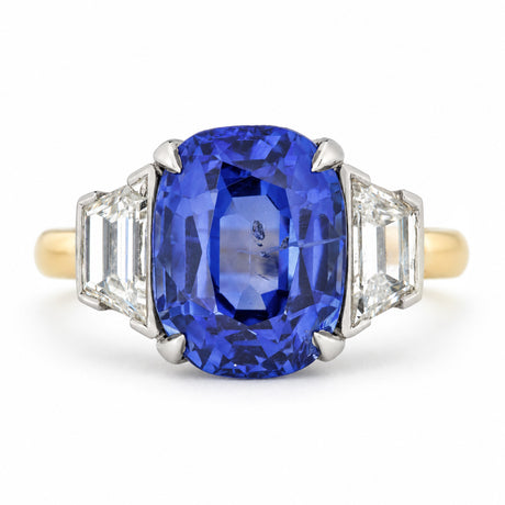 Front view of a vintage three-stone engagement ring featuring an oval blue sapphire flanked by two step-cut diamonds, set in platinum and yellow gold.