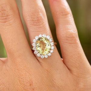 An up close image of a hand wearing a vintage engagement ring set with a green barrel and diamonds cluster style in yellow gold.