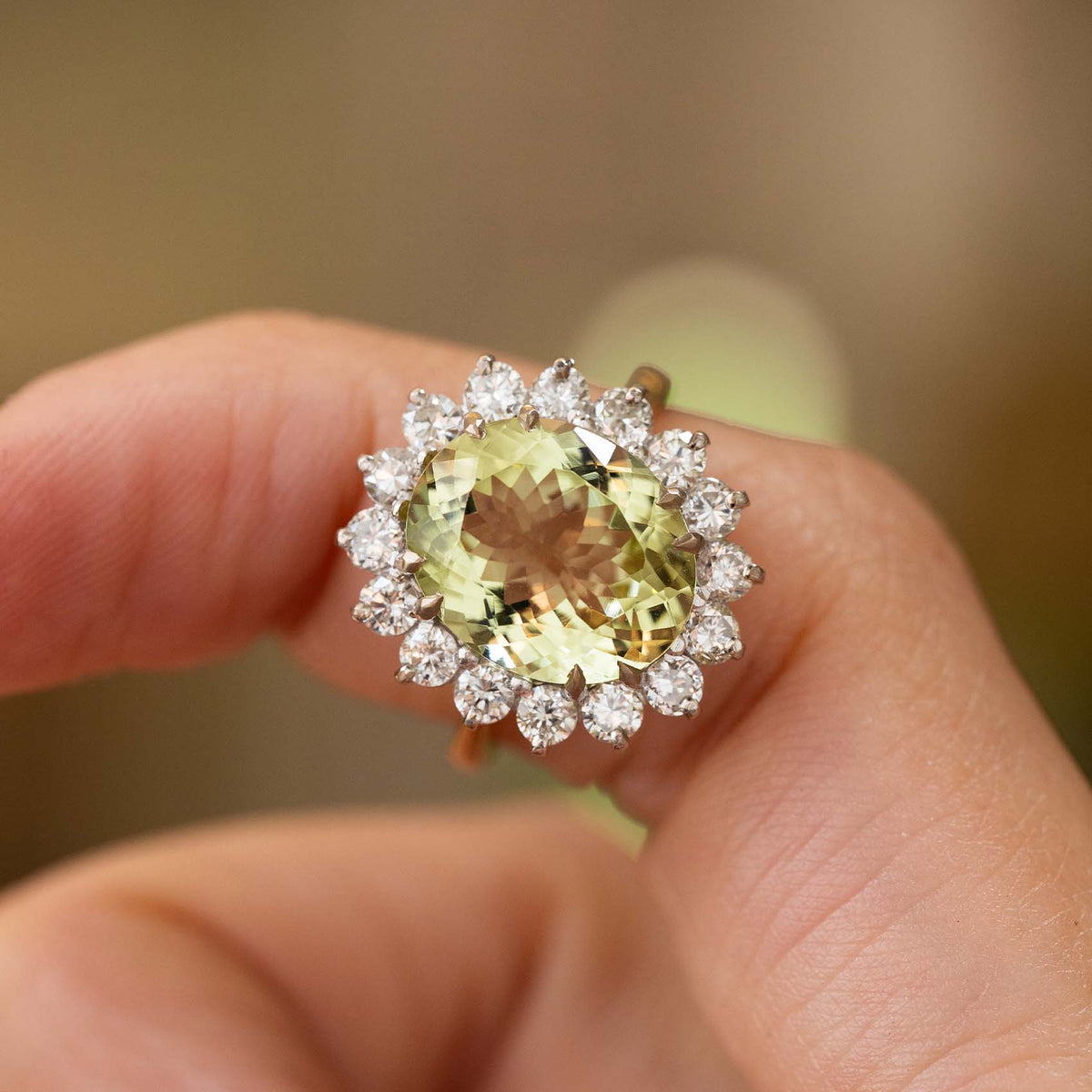 A close-up of a hand wearing a Vintage, 1960s Green beryl and diamond cluster engagement ring in gold.  