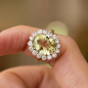 A close-up of a hand wearing a Vintage, 1960s Green beryl and diamond cluster engagement ring in gold.  