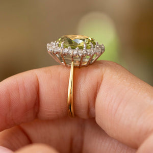 a Vintage, 1960s Green beryl and diamond cluster engagement ring in yellow gold with a white gold basket style setting shown balanced on a finger pictured from the side to show off the high profile and basket setting of the ring.