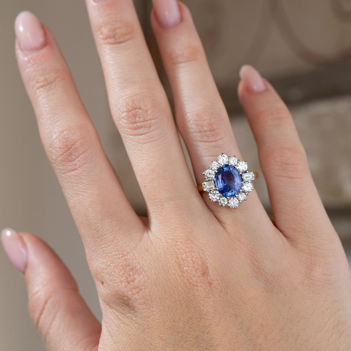 Vintage 1980s blue sapphire and diamond cluster ring worn on a hand, displaying its vibrant blue centre stone surrounded by a sparkling diamond halo.