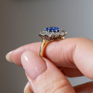 Side profile of a vintage 1980s blue sapphire and diamond cluster ring held between fingers, showing the elevated platinum cluster setting, diamond gallery and yellow gold band.