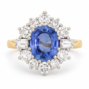 Vintage 1980s blue sapphire and diamond cluster ring in yellow gold and platinum, featuring an oval-cut blue sapphire surrounded by round brilliant-cut and baguette-cut diamonds.