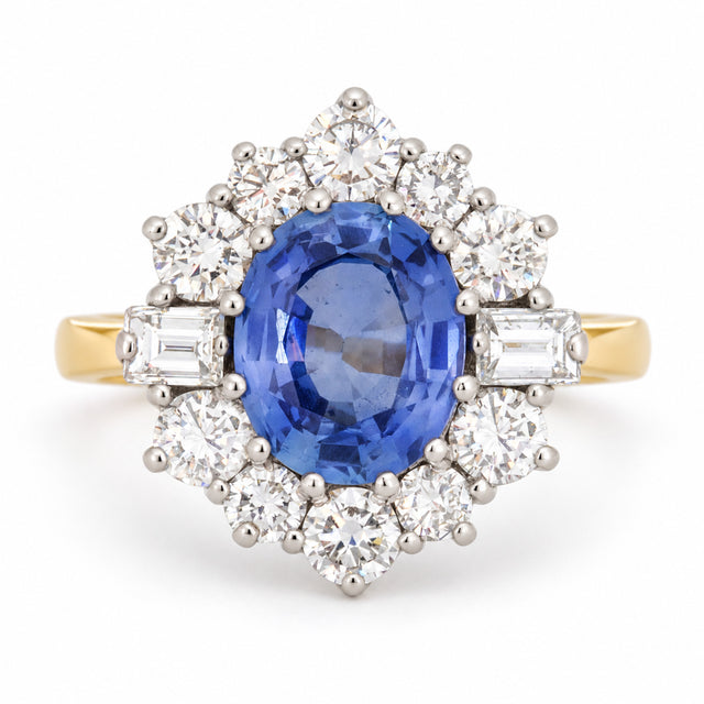 Vintage 1980s blue sapphire and diamond cluster ring in yellow gold and platinum, featuring an oval-cut blue sapphire surrounded by round brilliant-cut and baguette-cut diamonds.
