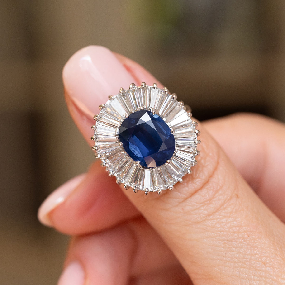 Vintage blue sapphire ballerina cluster ring held between the fingers, showing its radiating baguette diamonds and bold proportions.