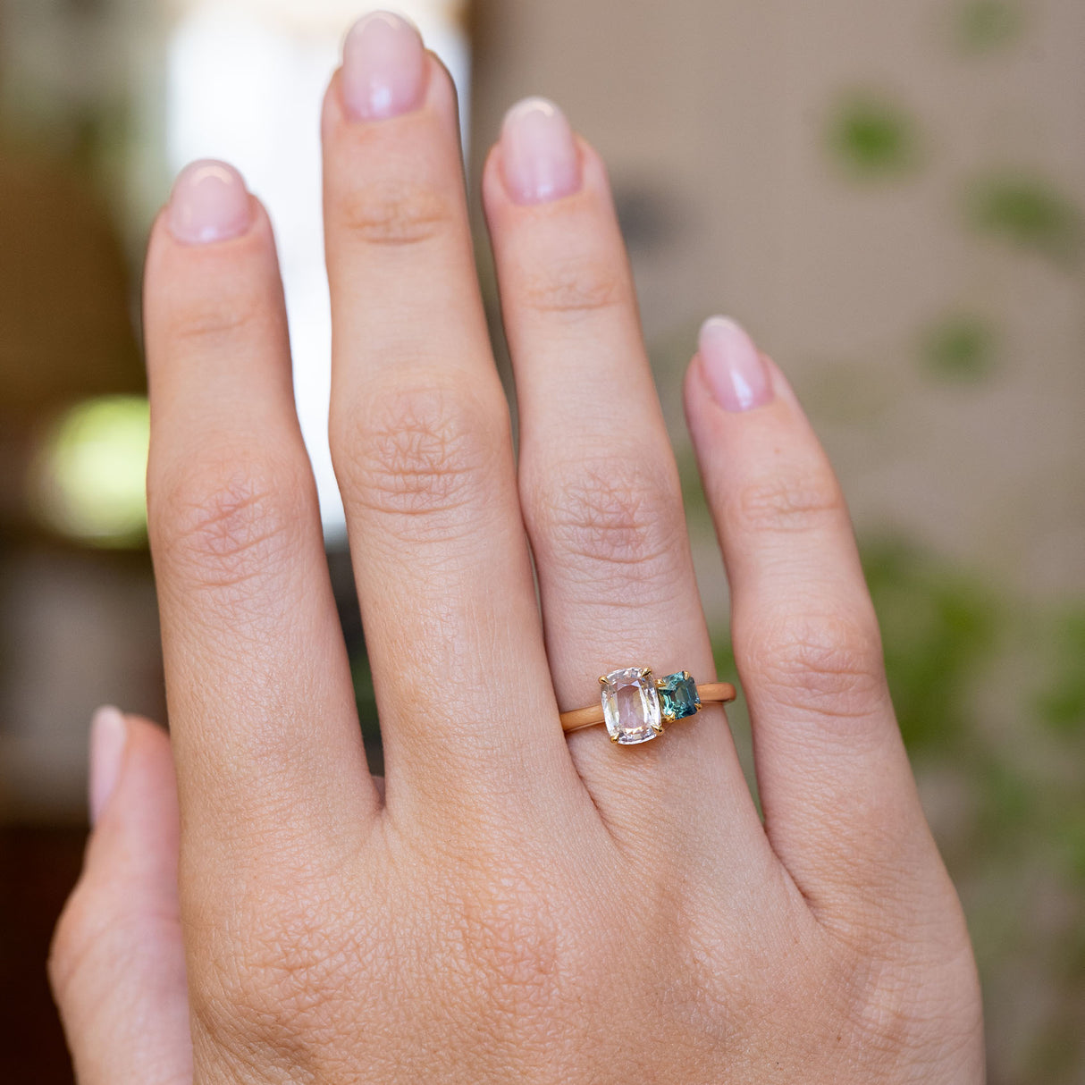 A photo of an Antique-inspired, colourless and blue Sapphire toi et moi two stone engagement ring on a yellow gold band worn on an outstretched hand to show off the proportions of the ring.