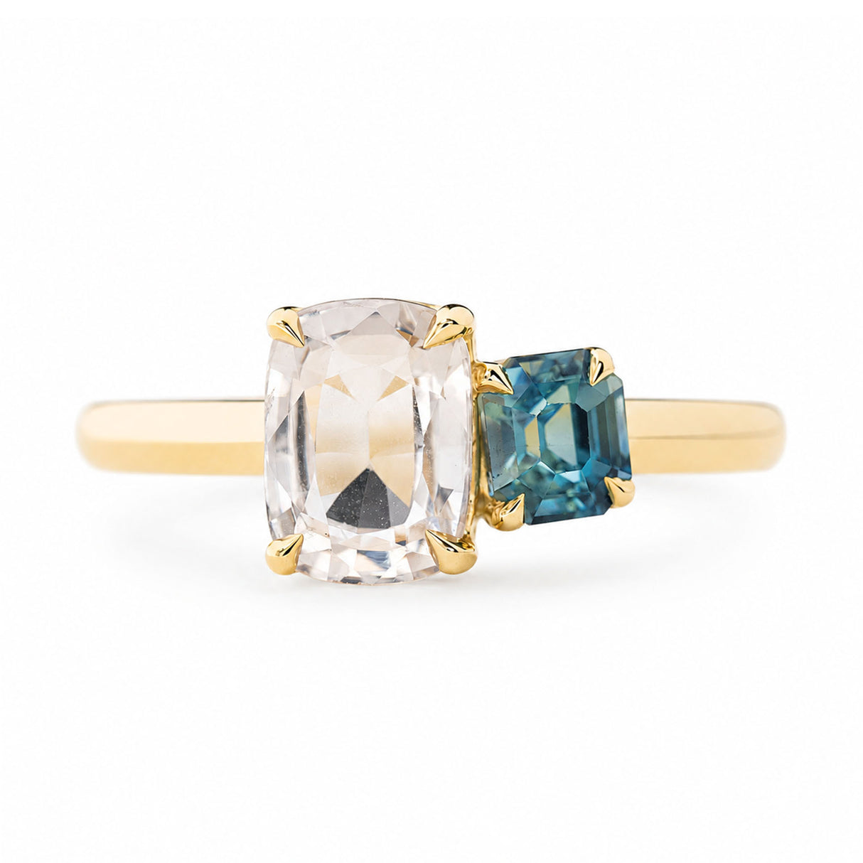 An antique-inspired yellow gold engagement ring featuring a large cushion-cut colourless sapphire and a smaller emerald-cut blue sapphire set on a plain white background.