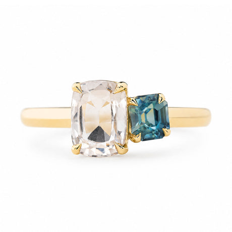 An antique-inspired yellow gold engagement ring featuring a large cushion-cut colourless sapphire and a smaller emerald-cut blue sapphire set on a plain white background.