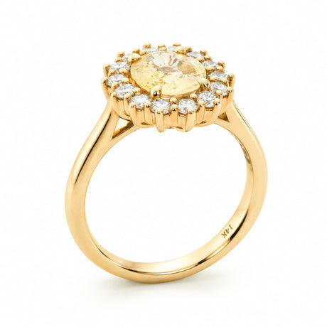 A vintage-inspired diamond halo engagement ring set to centre a pale yellow oval sapphire in 14ct yellow gold. 