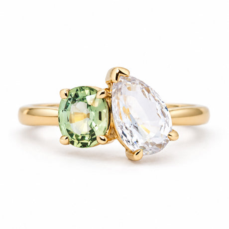 An antique-inspired, Sapphire toi et moi engagement ring in yellow gold featuring an oval-cut green sapphire and a pear-cut colorless sapphire.