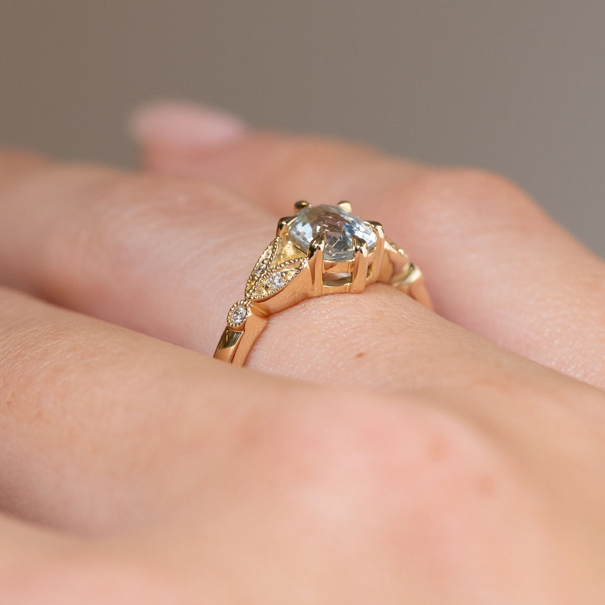 Side-angle view of the white sapphire engagement ring worn on a finger, highlighting the raised setting and intricate trefoil shoulders.
