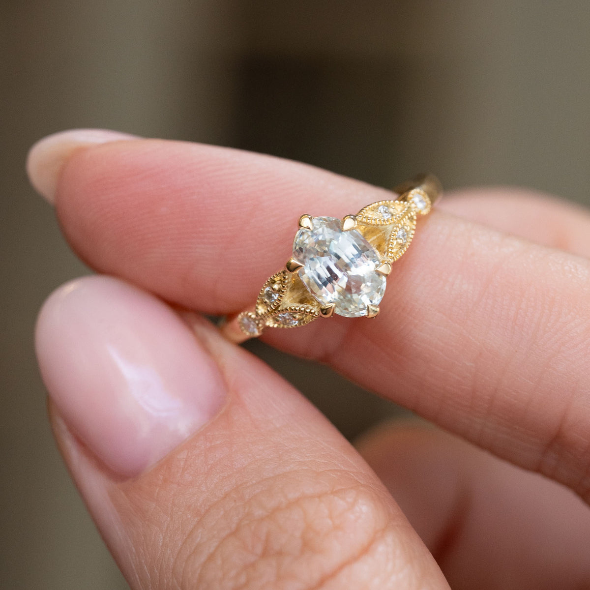 White sapphire and diamond ring held between the fingers, offering a detailed look at its symmetrical vintage-style design.