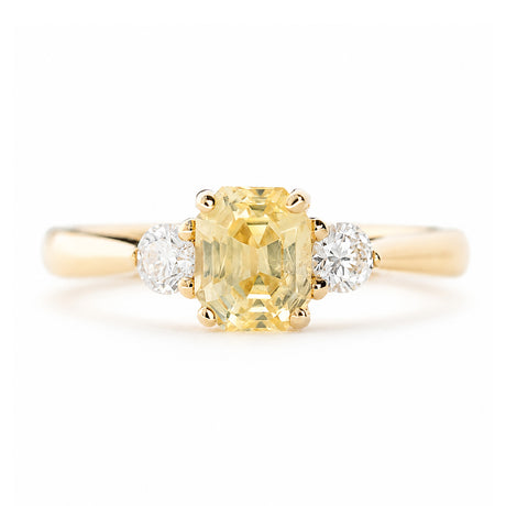 A close-up of a vintage-inspired, yellow sapphire and diamond three-stone engagement ring in yellow gold.