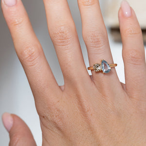 Sapphire and brown diamond engagement ring worn on a hand, showcasing its elegant asymmetric two-stone design.