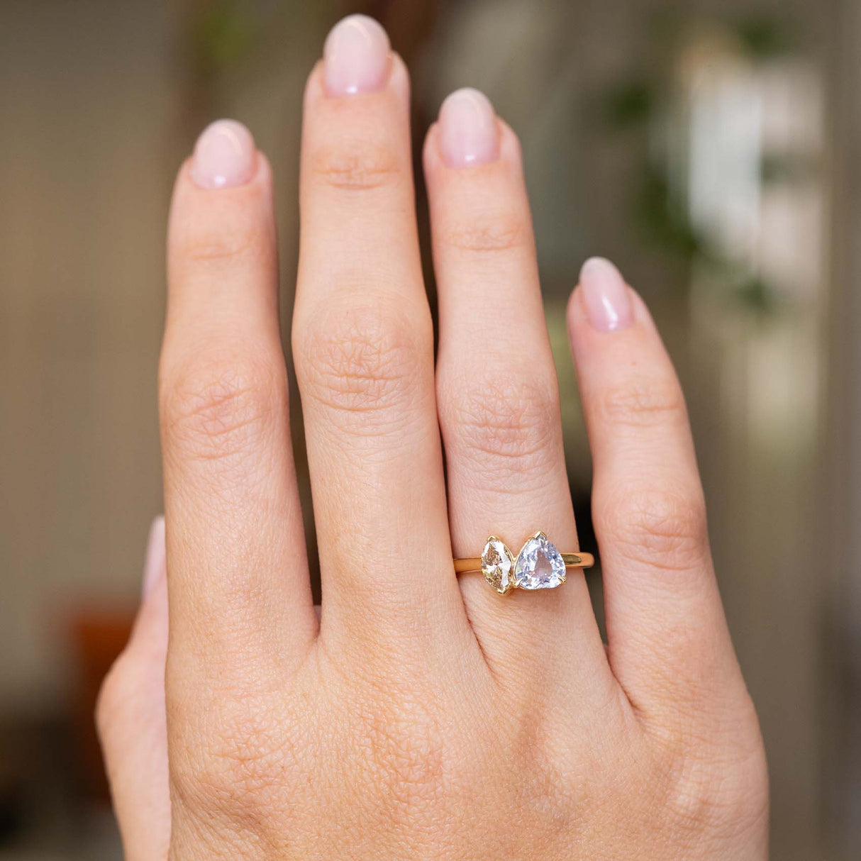 An outstretched hand wearing an antique-inspired toi et moi two stone engagement ring of a colourless sapphire and a brown marquise-cut diamond on a yellow gold band to show the proportions of the ring from a distance.