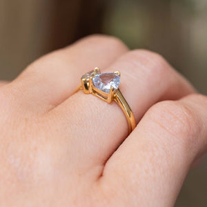 A hand wearing an antique-inspired, two stone toi et moi yellow gold engagement ring of a large colourless sapphire and a brown diamond seen from the side to showcase the open gallery and claw setting-style.