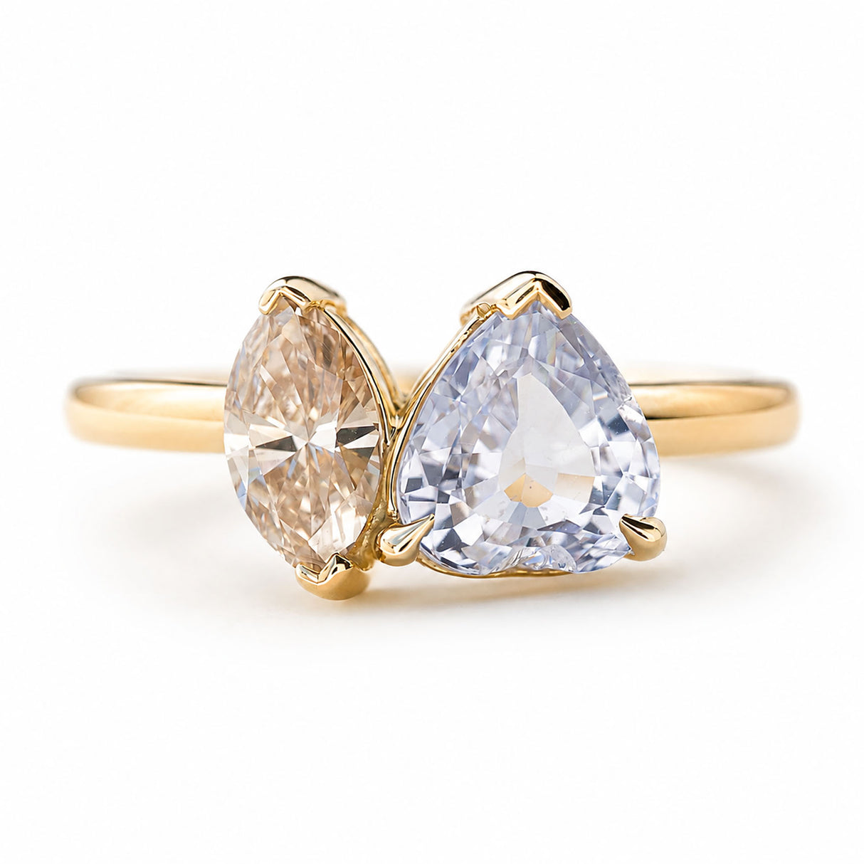 An antique-inspired yellow gold engagement ring featuring a large colourless sapphire and a brown marquise-cut diamond in a toi et moi two stone engagement ring against a plain white background.