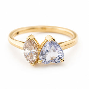 An antique-inspired yellow gold engagement ring shown against a white background at a slightly elevated angle featuring a large colourless sapphire and a brown marquise-cut diamond in a toi et moi two stone design.