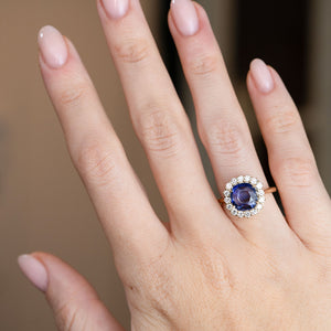 An elegant sapphire and diamond halo ring shown on a hand, demonstrating its proportions and striking oval centre stone.