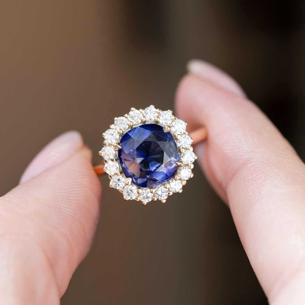 Close-up of the deep blue sapphire and brilliant diamond surround, held between fingers to showcase the gemstone's natural facets.