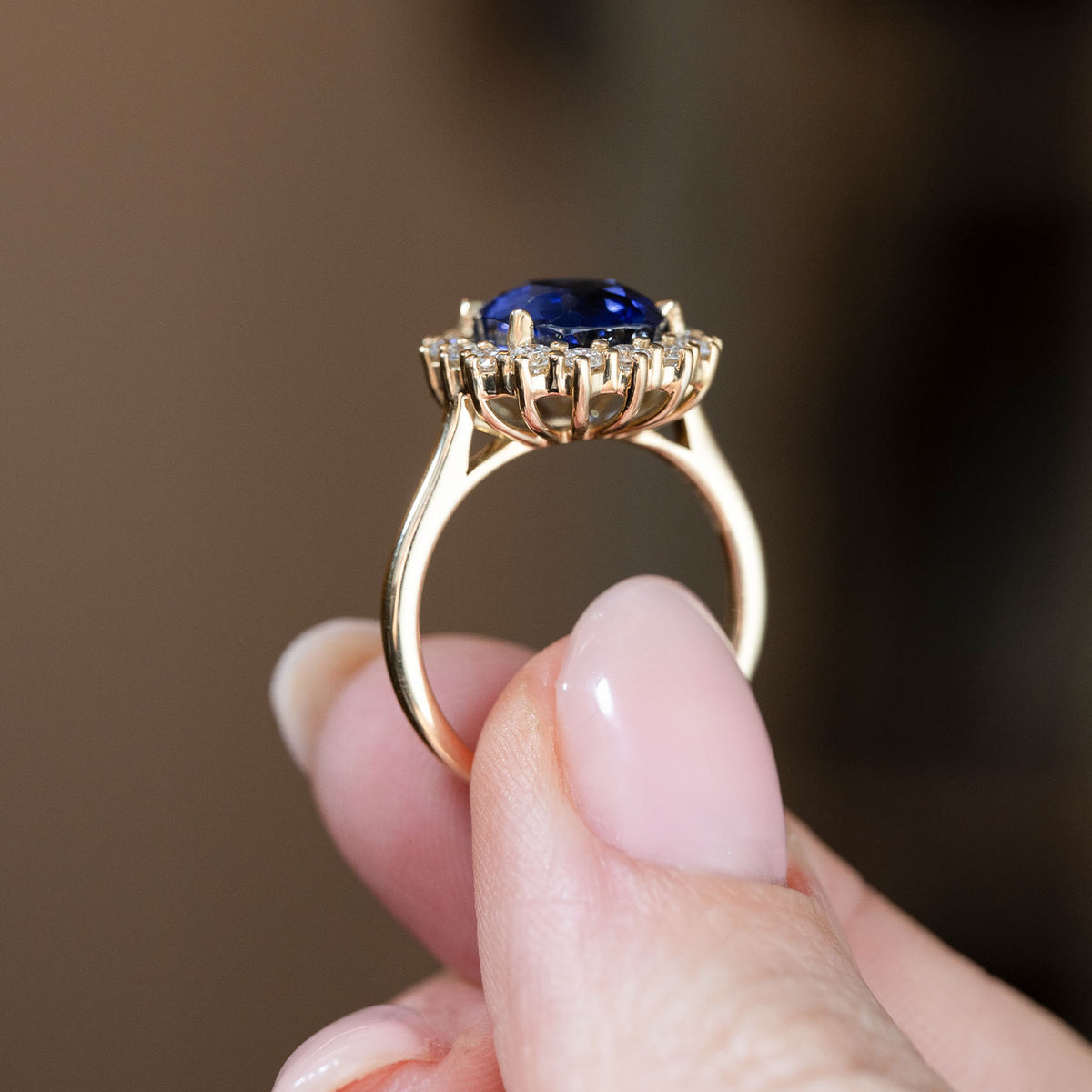 Side profile of the yellow gold engagement ring, revealing the elevated cluster setting and detailed gallery beneath the sapphire.