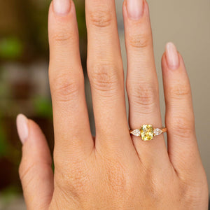 A hand shown from a distance wearing a yellow gold Antique-inspired, emerald-cut yellow sapphire and diamond trilogy engagement ring.