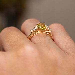 A close-up of a hand wearing an Antique-inspired, emerald-cut yellow sapphire and diamond three-stone ring in yellow gold, shown from the side.