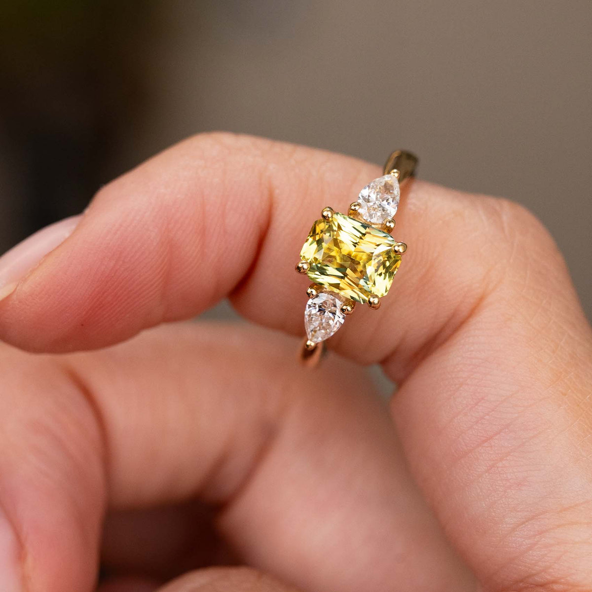 A close-up of a yellow gold Antique-inspired, emerald-cut yellow sapphire and diamond three-stone ring balanced on the finger.