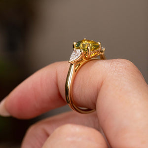 A hand wearing an Antique-inspired, emerald-cut yellow sapphire and diamond three-stone engagement ring on a yellow gold band.