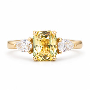 An antique-inspired, emerald-cut yellow-green sapphire and diamond three-stone ring in 14ct yellow gold.