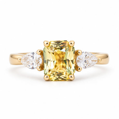 An antique-inspired, emerald-cut yellow-green sapphire and diamond three-stone ring in 14ct yellow gold.