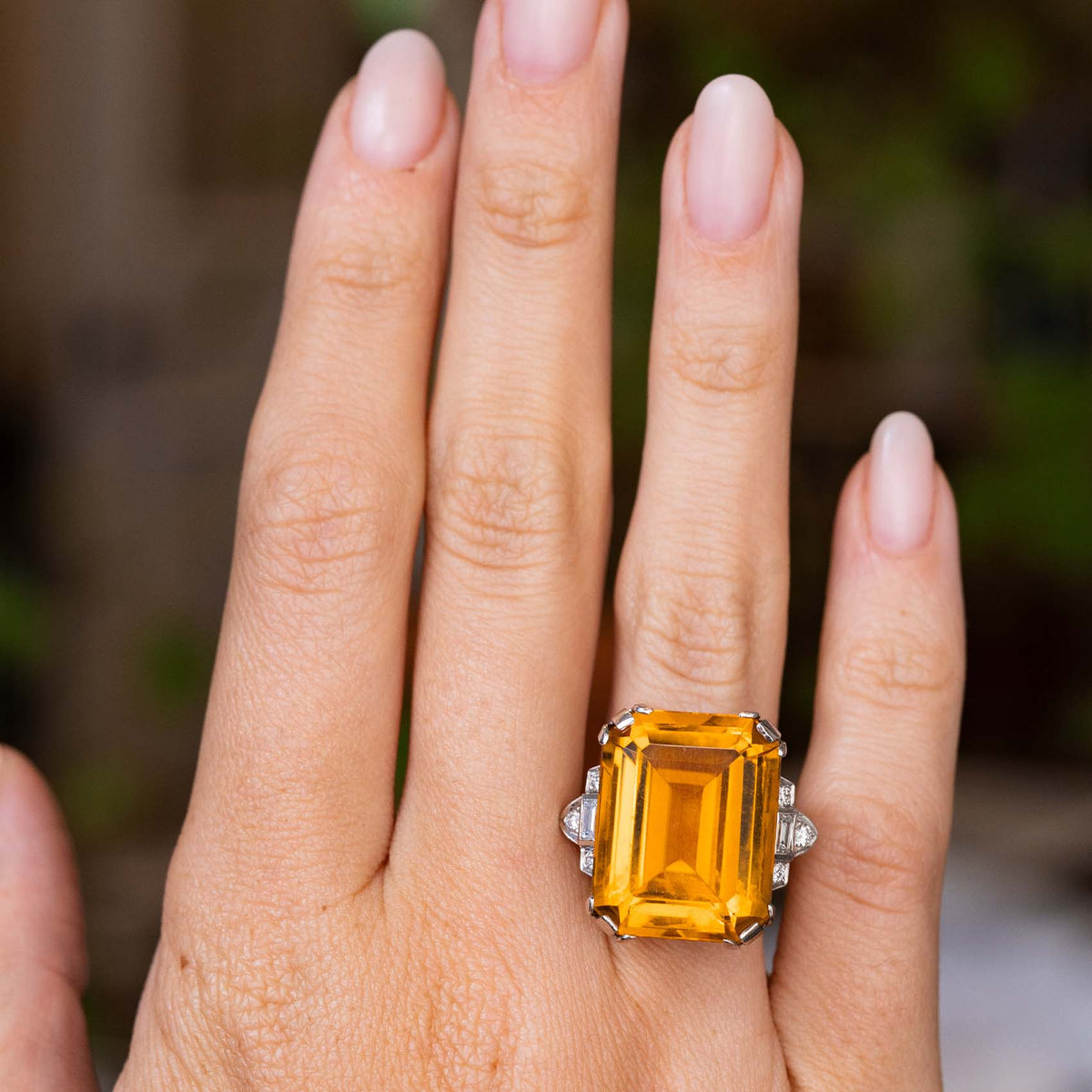 A hand wearing an Antique, Art Deco citrine and diamond cocktail ring in platinum shown from a distance to show off scale