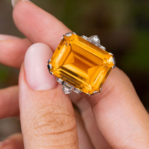 A close-up of a hand holding a platinum Antique, Art Deco citrine and diamond cocktail ring.