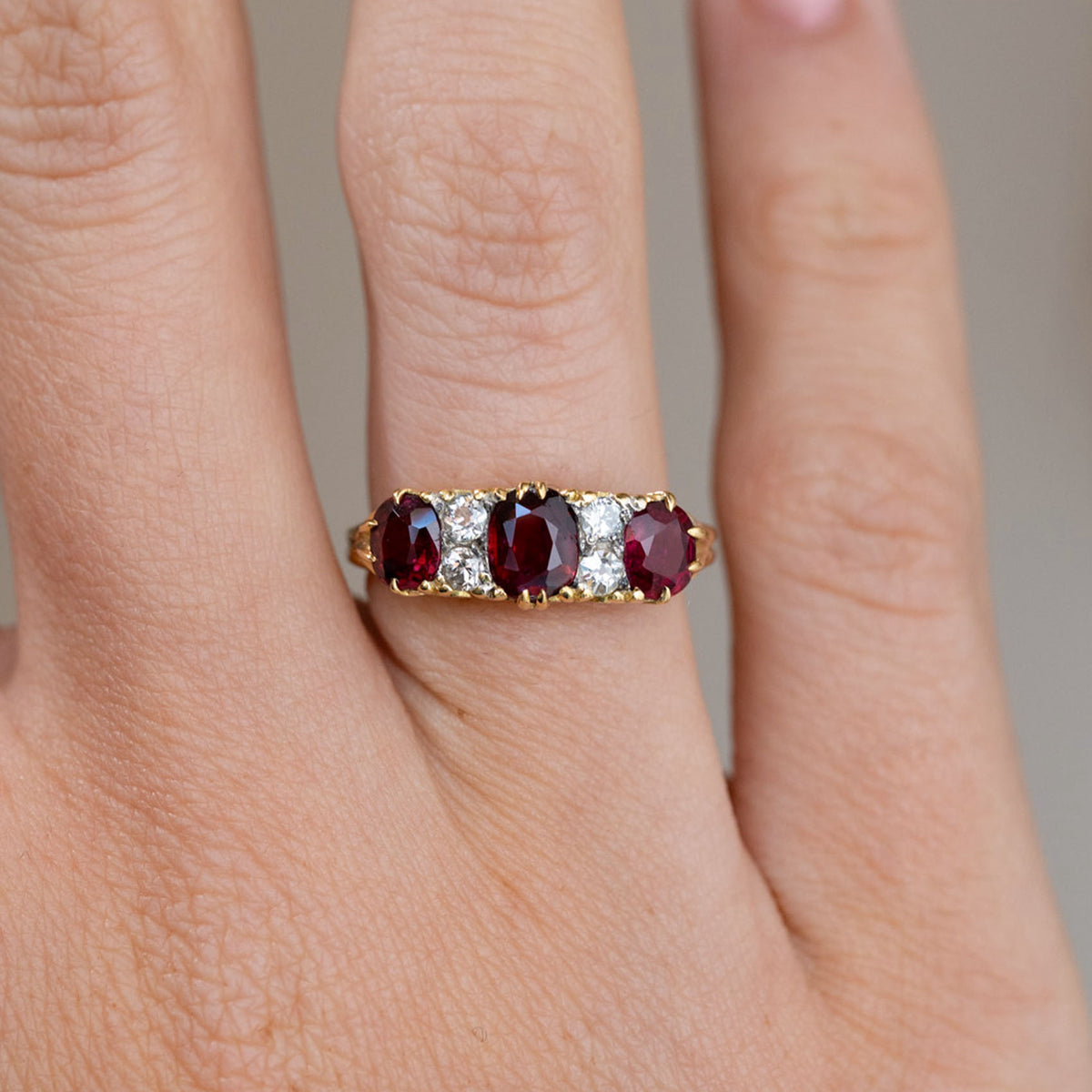 Close finger detail highlighting three deep red rubies, bright old-cut diamonds and warm yellow gold claws.