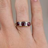 Close finger detail highlighting three deep red rubies, bright old-cut diamonds and warm yellow gold claws.