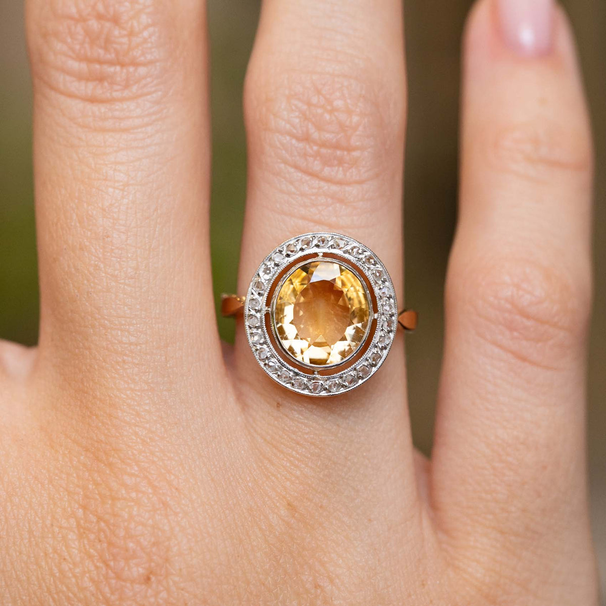 Detailed hand view of an antique citrine and diamond ring, displaying the decorative platinum halo and yellow gold band.