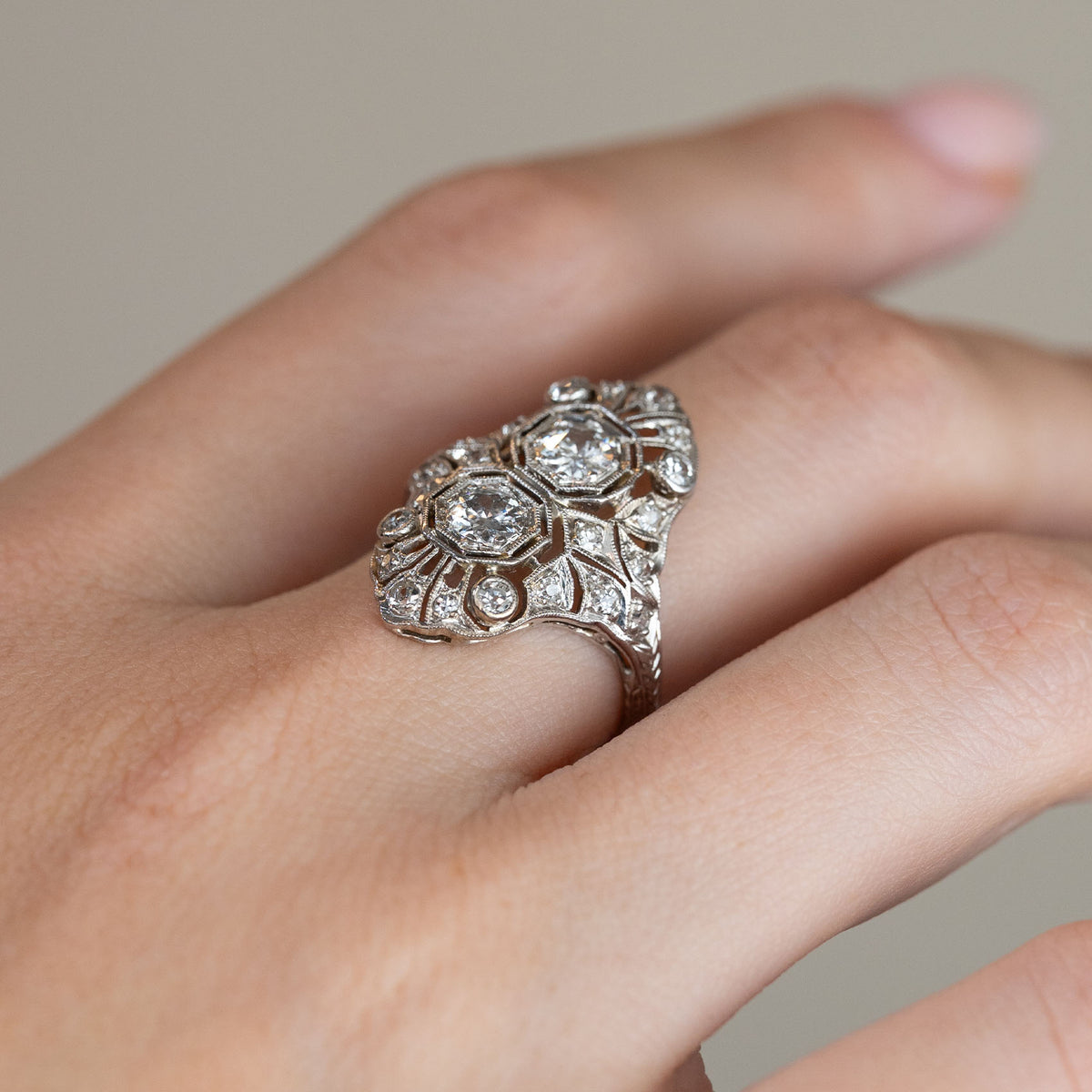 Side-angle view of the antique diamond ring worn on a hand, revealing the raised decorative setting and detailed platinum shoulders.