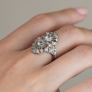 Side-angle view of the antique diamond ring worn on a hand, revealing the raised decorative setting and detailed platinum shoulders.
